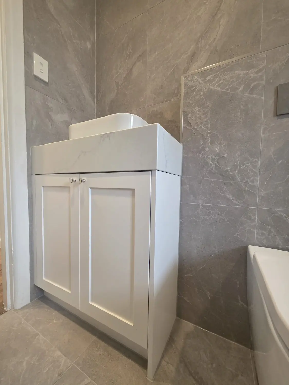 Stone top bathroom vanity with shaker doors and grey tiles in an East Melbourne apartment by Northside Joinery Melbourne
